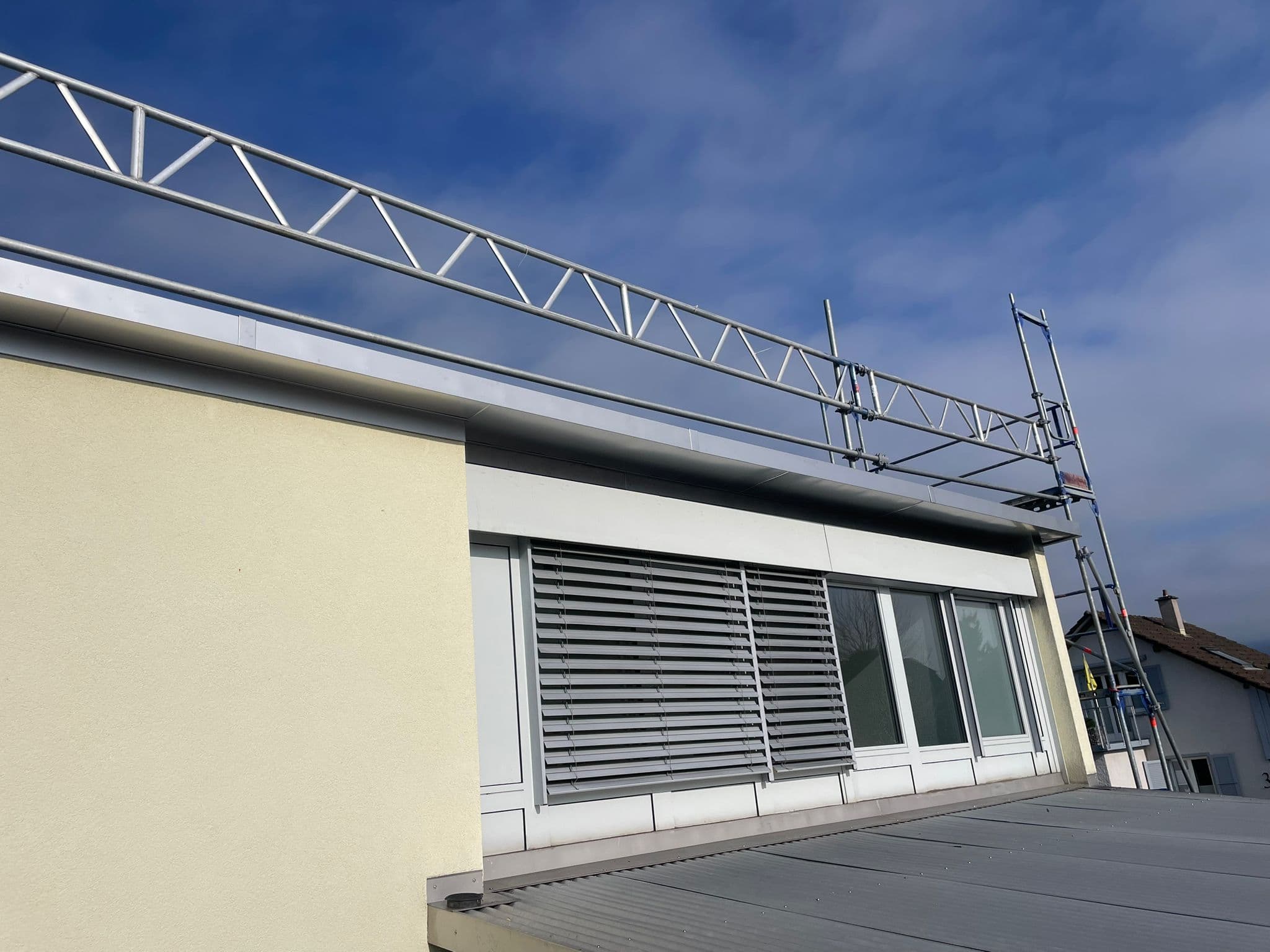 Eingerüsteter Dachrand mit Aluminium-Attika unter blauem Himmel