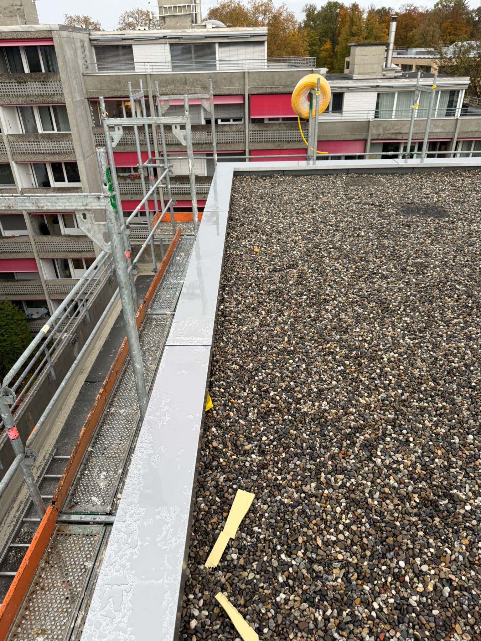 Aluminium-Attika auf Flachdach mit Wohnsiedlung im Hintergrund